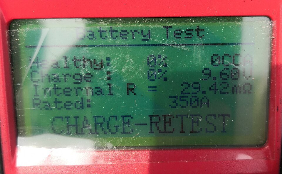 Battery tester screen displaying a charge and retest instruction
