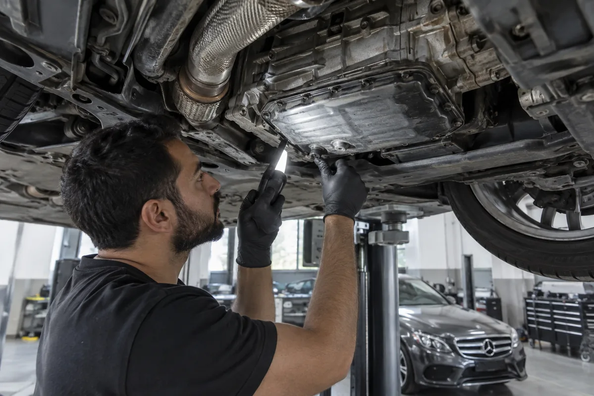 Technician inspecting a Mercedes transmission sump on a workshop lift